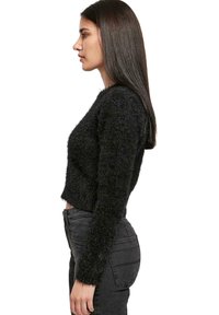 Maglione nero e peloso a maniche lunghe, con una texture morbida. Abbinato a jeans scuri e aderenti; vista di profilo.