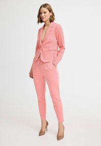 Rosa maßgeschneiderte Blazerjacke mit Reverskragen und vorderen Taschen, kombiniert mit passenden, schmal geschnittenen Joggerhosen. Glattes Material, minimalistisches Design.