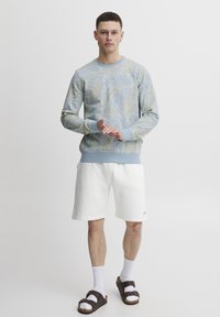 Lysblå sweatshirt med bladmønster, ribbede manchetter og kant. Kombination med hvide shorts, hvide sokker og brune sandaler. Strømlinet design.