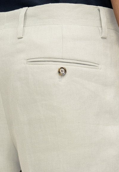 Pantalones de lino de color beige claro con un bolsillo trasero y cierre de un solo botón. Presentan un tejido texturizado y un detalle sutil de costuras.