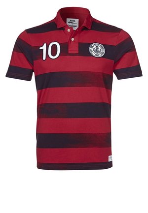 Polo rayé rouge et bleu foncé avec le numéro 10 sur la poitrine gauche et un badge circulaire de club de football sur la poitrine droite.