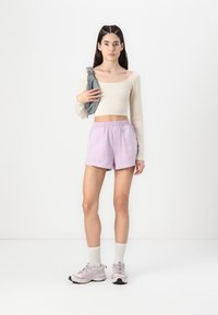 Lys beige langærmet crop top, lilac shorts med snor, grå crossbody taske, lyserøde sneakers med sorte såler, hvide ankelstrømper.