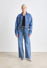 Τζάκετ από τζιν με δύο εμπρός τσέπες, κοντή σχεδίαση, ανοιχτό μπλε χρώμα, συνδυασμένο με φαρδιά τζιν και μαύρη ζώνη με ασημί αξεσουάρ.