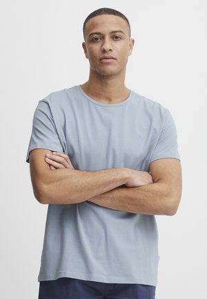 T-shirt en coton bleu clair avec un col ras du cou, des manches courtes et un petit logo sur la poitrine. Texture douce et coupe décontractée.
