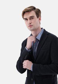 Schwarzer Cord-Blazer mit Revers und Kerbkragen, kombiniert mit einem hellblauen, strukturierten Hemd. Glattes, elegantes Design mit dezenten Akzenten und Knopfdetails.