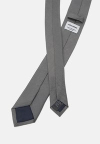 Grå slips med en elegant design, med en texturerad undersida i marinblått, och en varumärkesetikett upptill, tillverkad av vävt tyg.