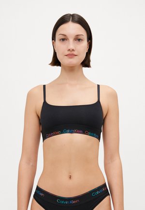 Black cotton bralette with thin straps, featuring a contrasting multicolored "Calvin Klein" logo band along the bottom. Smooth texture.