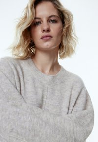 Hellgrauer Strickpullover mit rundem Ausschnitt, lockerer Passform und langen Ärmeln. Weiche Textur mit dezentem Muster.