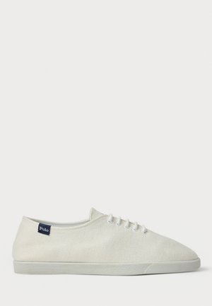 Sneaker bassa in tela bianca con lacci bianchi, suola in gomma piatta e piccolo etichetta blu navy con la scritta "Polo" vicino al tallone sul lato esterno.