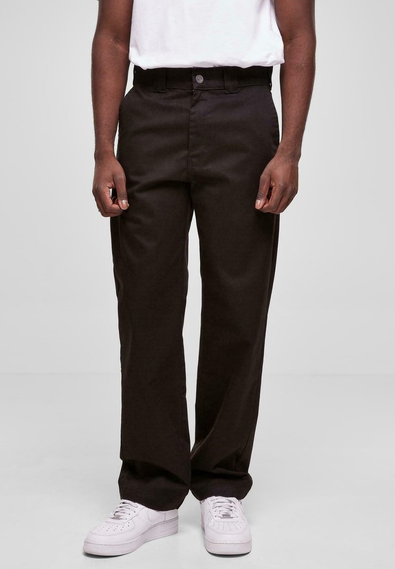 Pantalon droite en coton mélangé de couleur marron foncé. Doté d'une fermeture par bouton, de passants pour ceinture et de poches latérales. Associé à des baskets blanches.