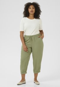 Light olive green, elastic-waist pants with a relaxed fit and adjustable drawstring. Paired with a fitted white short-sleeve top.