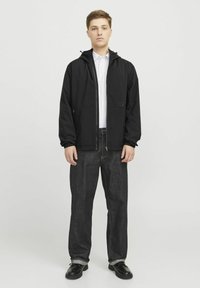 Zwarte, lichtgewicht jas met een rits aan de voorkant en een capuchon, gecombineerd met donkerdenim jeans. Zwarte schoenen maken de outfit compleet. Eenvoudig ontwerp, geen patronen.