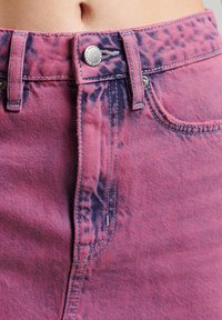 Rosa denimkjol med ett tie-dye-mönster, med metallknappstängning, bältesöglor och kontrasterande sömmar längs kanten.