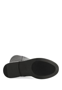 Czarna gumowa podeszwa buta z teksturowaną powierzchnią i pionowymi paskami. Cholewka ma gładki, pikowany wzór z zaokrąglonym czubkiem.