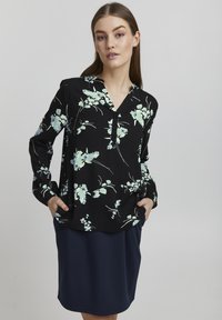 Svart blommig blus med ljusblå och gröna blommor, långa ärmar, knappslå, kombinerad med en enkel marinblå kjol. Slät tygtextur.