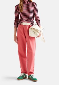 Randig rosa och svart polotröja, högmidjade rosa byxor, vit bälte och gröna sneakers med vita detaljer, tillsammans med en mönstrad väska.