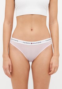 Baltās kokvilnas apakšbikses ar plānām rozā horizontālām svītrām, ar zīmola elastīgu jostasvietu, kurā ir izdrukāts "TOMMY HILFIGER".