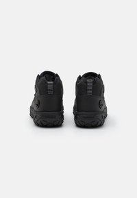 Black Timberland shoes with a textured synthetic material, high ankle support, and rugged rubber soles, featuring a logo and rear pull tab.