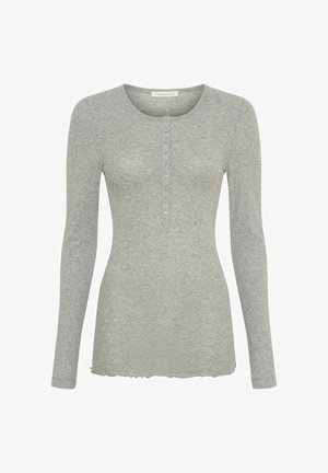 Vaaleanharmaa pitkähihainen paita, joka on valmistettu pehmeästä, teksturoidusta kankaasta. Siinä on pyöreä pääntie ja seitsemän nappia edessä. Kaareva helma.