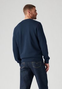 Marineblauwe sweatshirt met een ronde hals, ribbelmanchetten en -zoom, gecombineerd met donkerblauwe jeans met zichtbare stiksels en achterzakken.