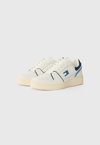 Baskets blanches avec des accents bleus, tige en cuir lisse, boîte à orteils perforée, semelle en caoutchouc solide, et marque bleue contrastante sur le côté.