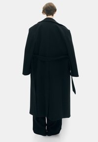 Zwarte wollen overjas met een brede kraag, lange mouwen en een gestrikte taille, gekenmerkt door een zachte textuur en een strakke, rechte silhouet.