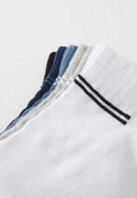 Rôzne ponožky v modrej, sivej, čiernej a bielej farbe. Biela dvojica má čierny prúžok. Materiály sa zdajú byť z bavlnenej zmesi s textúrovaným povrchom.