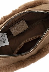 Interno di una borsa in pelle marrone con soffice bordo in pelliccia. Presenta una chiusura con zip, fodera in tessuto e un'etichetta con informazioni sul marchio e cura.