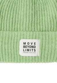 Jasnozielona dzianinowa czapka z pionowym prążkowaniem, z prostokątną białą metką z napisem "MOVE BEYOND LIMITS" czarnym tekstem.