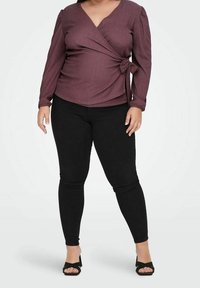 Bordeaux wikkelblouse met lange pofmouwen en een strik in de taille, gecombineerd met zwarte strakke jeans en zwarte open-toe hakken.