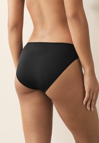 Fekete, varrásmentes hipster alsónemű, puha textúrával, sima derékrésszel és finom csipke díszítéssel a széleken.