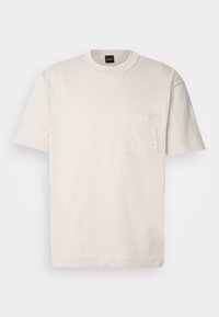 Ljusbeige t-shirt med kort ärm i bomull, med en bröstficka som har en diskret logotagg. Klassisk rund halsringning, avslappnad passform.