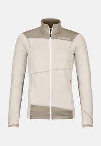 Beige Fleece-Jacke mit kontrastierendem taupefarbenem Schulterbereich, durchgehendem Reißverschluss und auffälligen Nahtdetails. Verfügt über zwei Seitentaschen.