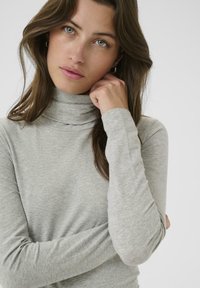 Helehall turtleneck-särk pehmest ja tekstuuriga kangast, mis on varustatud pikkade varrukatega ning tihedalt kinnitub kaela ümber.