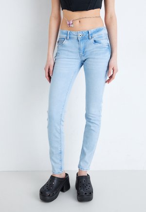 Jeans skinny de color azul claro con un acabado desgastado, cinco bolsillos y herrajes de metal, combinados con zuecos gruesos negros.