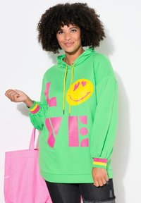 Felpa verde con cappuccio, decorata da un grande sorriso giallo e con la scritta "LOVE" in rosa. Presenta dettagli colorati sulle maniche e una vestibilità comoda.