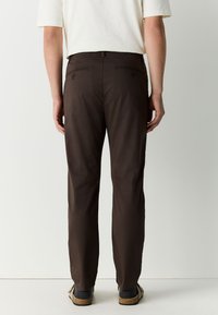 Men's brown trousers with a classic fit, featuring two back pockets, a smooth texture, and a straight leg design, paired with casual footwear.