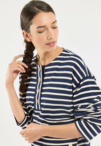 Navy and cream striped top featuring a rounded neckline, wooden buttons, and three-quarter sleeves with a relaxed fit.