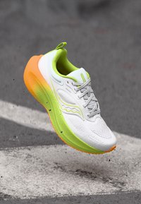 Chaussure de sport blanche avec une tige en mesh, des accents vert néon, une semelle extérieure orange et une semelle texturée pour l'adhérence. Dotée d'un design léger et de lacets.