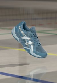 Lys blå treningssko med mesh-overdel, hvite detaljer og en teksturert såle. Har polstret krage og snøring.