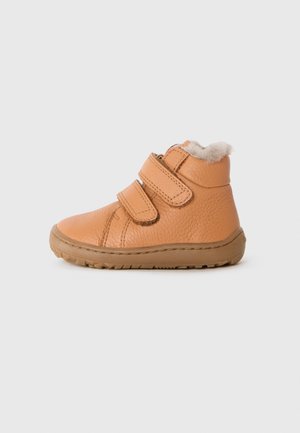 Botte pour tout-petit en cuir couleur fauve avec deux sangles Velcro, semelle en caoutchouc marron et doublure blanche douce, présentée sur un fond gris uni.