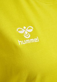 Limegrøn t-shirt i blødt materiale med et broderet hvidt logo af en bi og ordet "hummel" under designet.