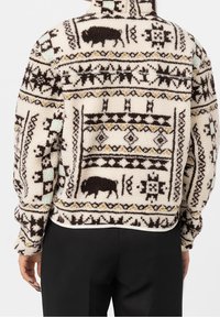 Polarowy sweter z kremową bazą, zdobiony geometrycznym wzorem w ciemnym brązie, żółtym i niebieskim. Wyrazisty motyw bawoła oraz zamek przy kołnierzu.