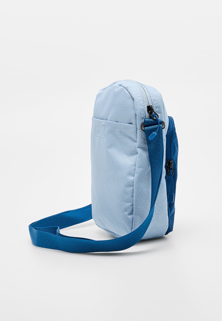 Bolso bandolera de tela azul claro con un bolsillo con cremallera, correa azul ajustable, forma rectangular y superficie texturizada.
