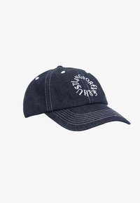 Denim baseball cap i mørkeblå med hvid syning og øjler. Har cirkulær, hvid broderet tekst på fronten.