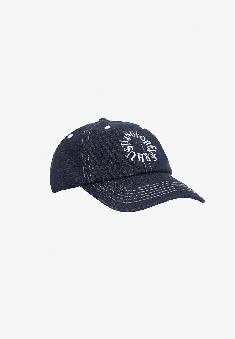 Denim baseball cap i mørkeblå med hvid syning og øjler. Har cirkulær, hvid broderet tekst på fronten.