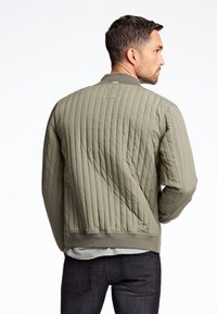 Chaqueta bomber acolchada en verde oliva, con un cuello y puños de canalé, textura suave y un sutil detalle de costura.