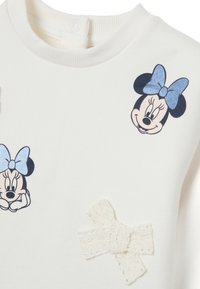 Sweatshirt blanc avec col côtelé, ornée de motifs imprimés de Minnie Mouse et d'un détail en forme de nœud texturé blanc. Matière douce, coupe décontractée.