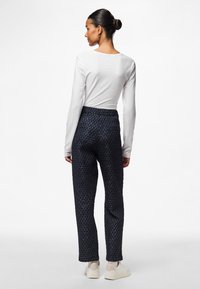 Pantaloni a fantasia blu scuro in tessuto testurizzato; cintura elastica; indossati con una maglietta bianca a maniche lunghe e sneaker di colore chiaro.