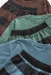 Vier Kleidungsstücke in verschiedenen Texturen: ein braunes Karomuster mit schwarzen Akzenten, ein einfarbiges Teal, ein strukturiertes Grün und ein blauer Strukturstoff, alle mit gerippten Kragen.